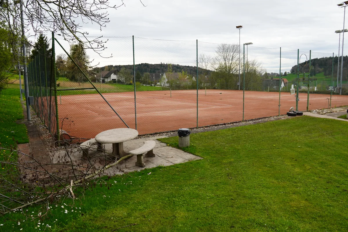 Zu sehen ist ein rötlicher Tennisplatz.